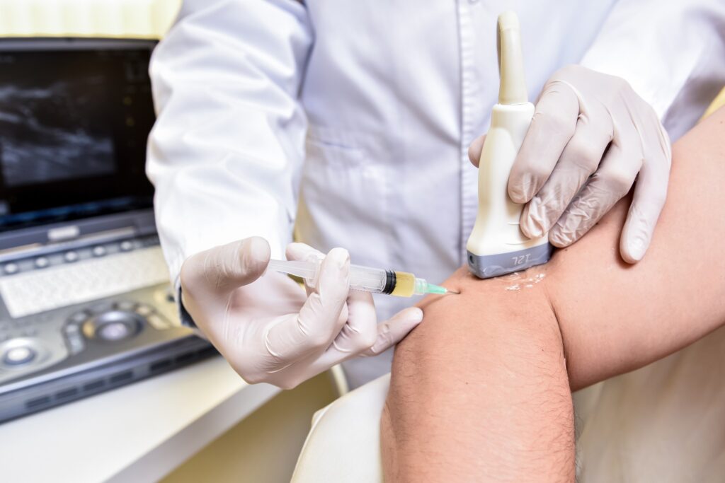 Lekarz radiolog Marcin Paśnik wykonujący iniekcję do stawu pod kontrolą ultrasonografu w gabinecie Synovia Warszawa