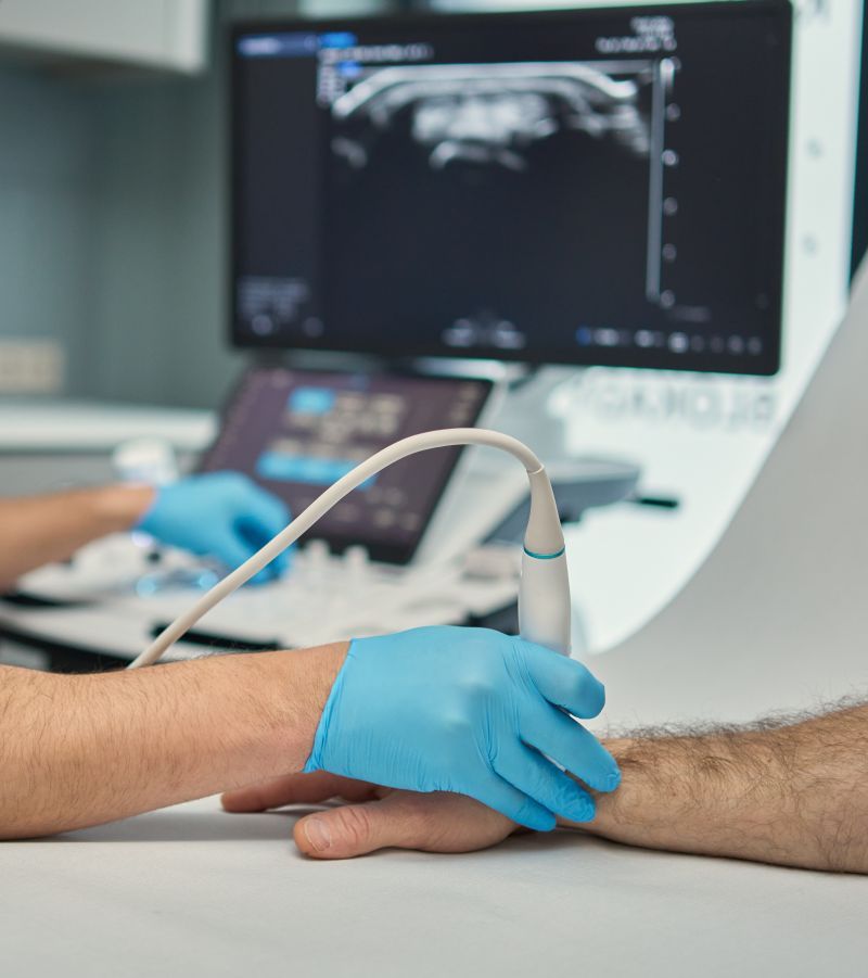 Lekarz wykonujący badanie USG ręki z widocznym obrazem ultrasonograficznym na monitorze